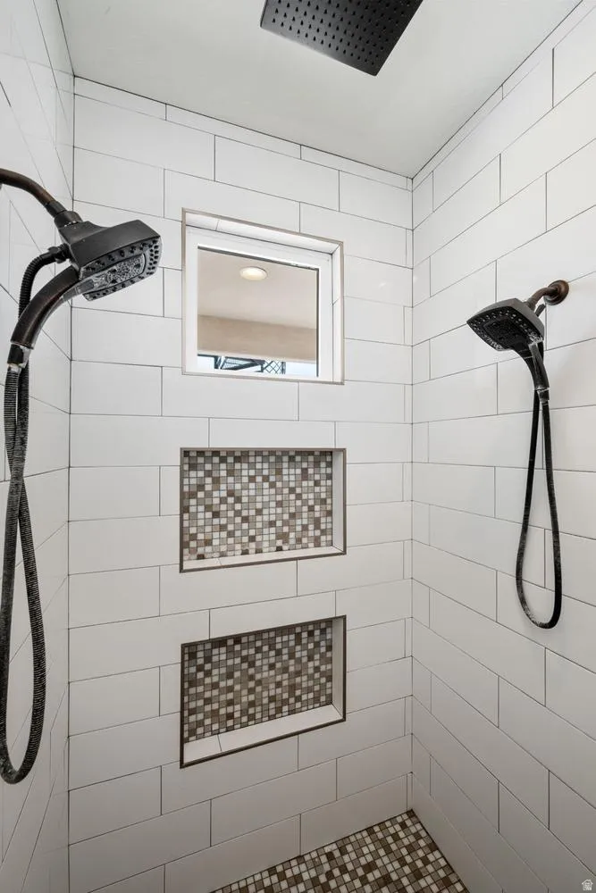 Shower featuring subway tile walls, two recessed niches with mosaic tile backing, a rain shower head, and a handheld shower fixture