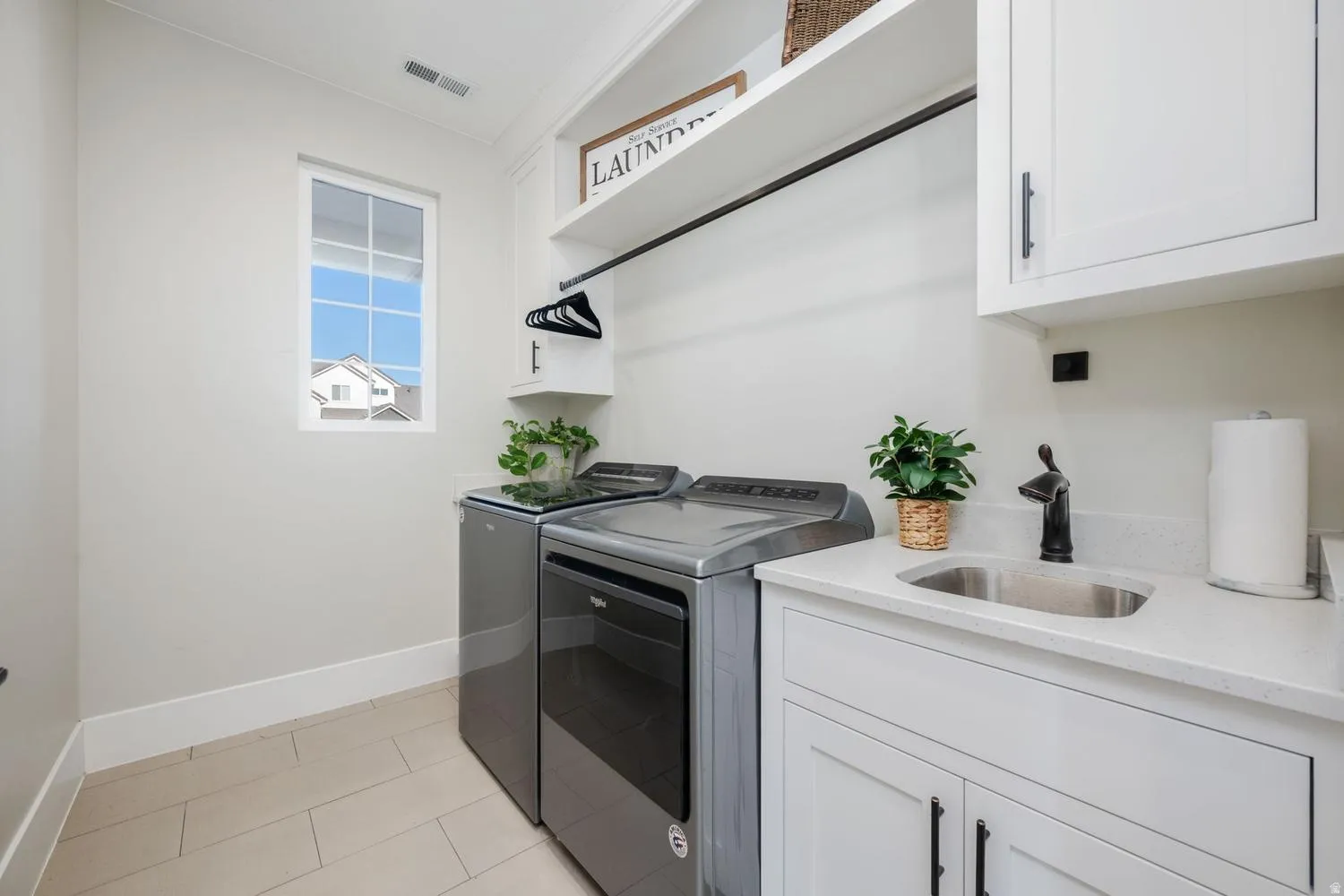 Dedicated laundry area featuring a utility sink with a black faucet, white cabinetry with black hardware, and ample counter space