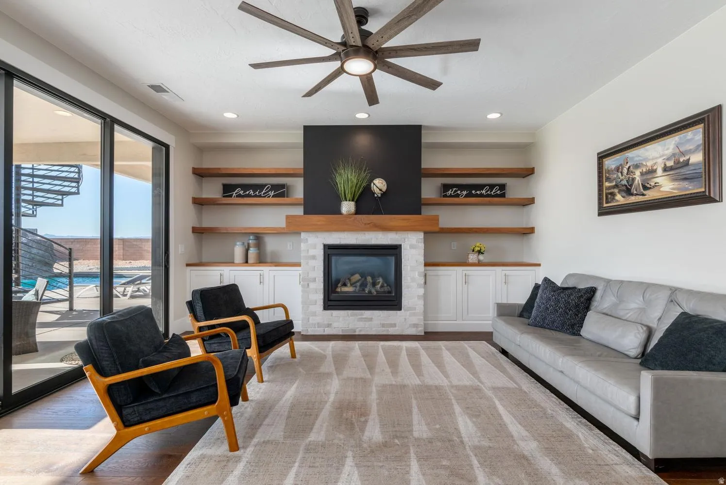 Living area featuring a floor-to-ceiling fireplace with stone surround, custom built-in cabinetry, and wood-finish floating shelves