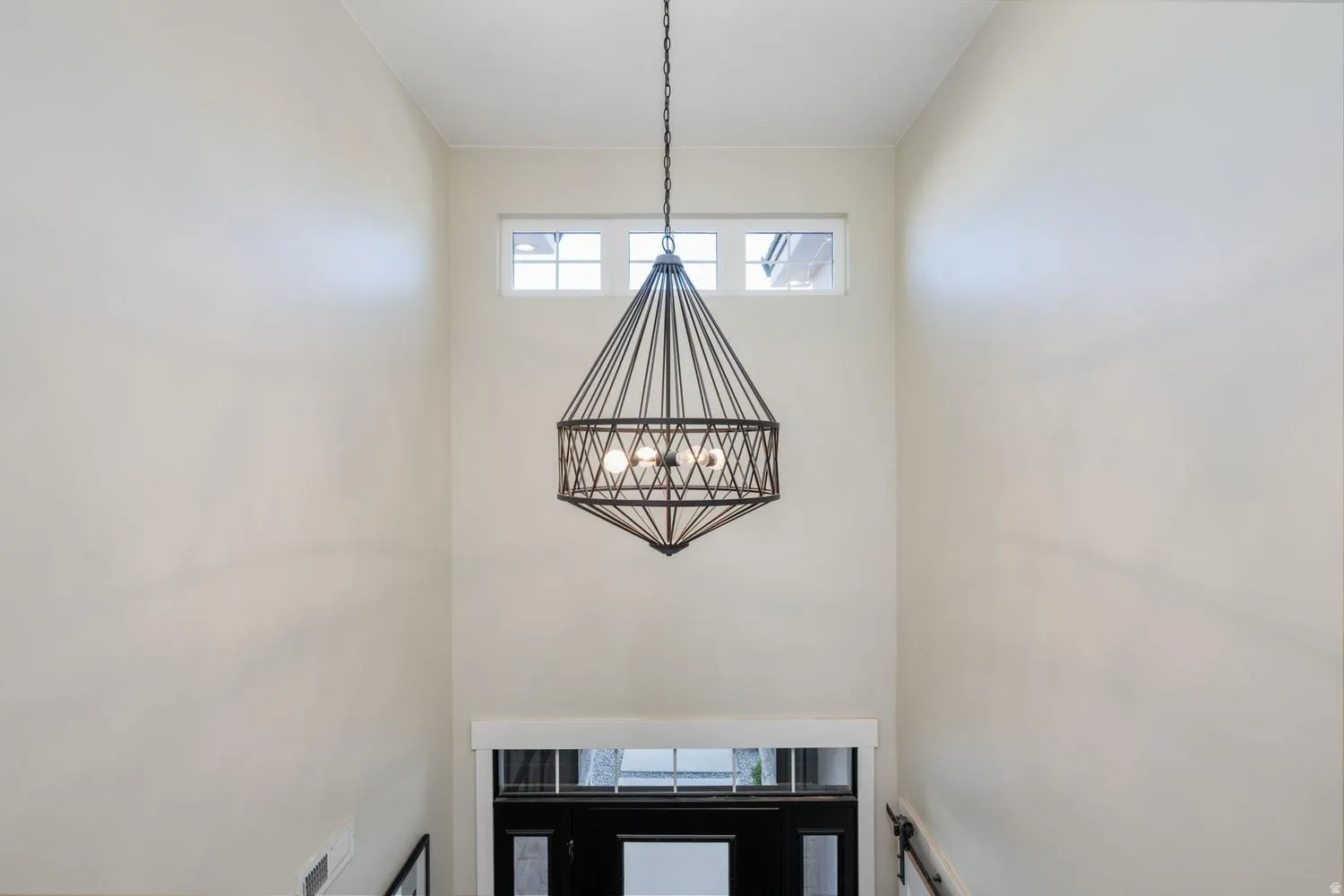 Two-story entryway featuring a geometric chandelier, transom windows, and a dark-paneled door with glass inserts