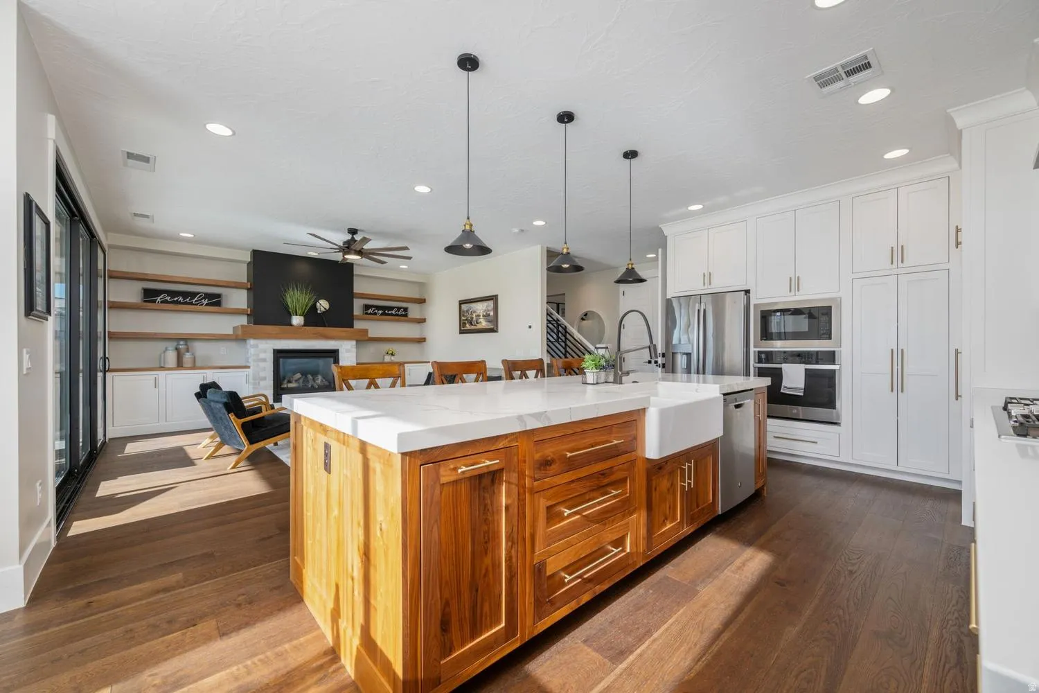Open-concept living space featuring a central kitchen island with a farmhouse sink and wood-finish cabinetry, a full suite of stainless steel appliances, and wood-finish flooring