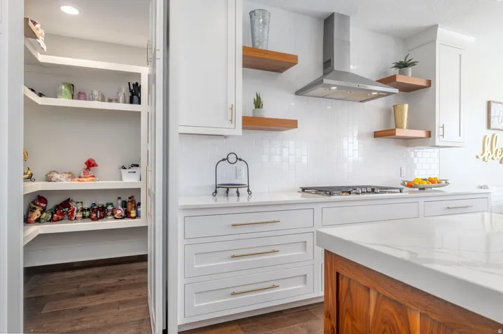 Modern kitchen featuring white shaker cabinetry with gold-tone hardware, white subway tile backsplash, and a stainless steel range hood