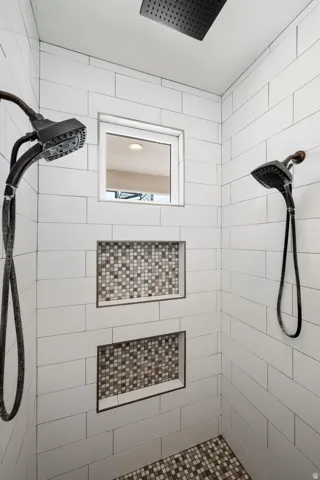 Shower featuring subway tile walls, two recessed niches with mosaic tile backing, a rain shower head, and a handheld shower fixture