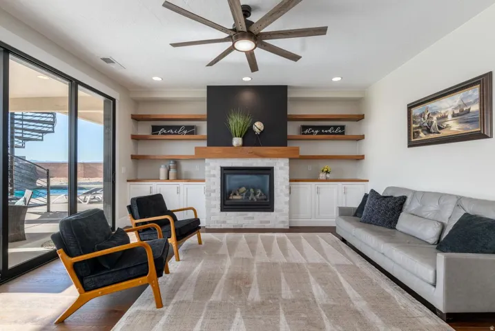 Living area featuring a floor-to-ceiling fireplace with stone surround, custom built-in cabinetry, and wood-finish floating shelves