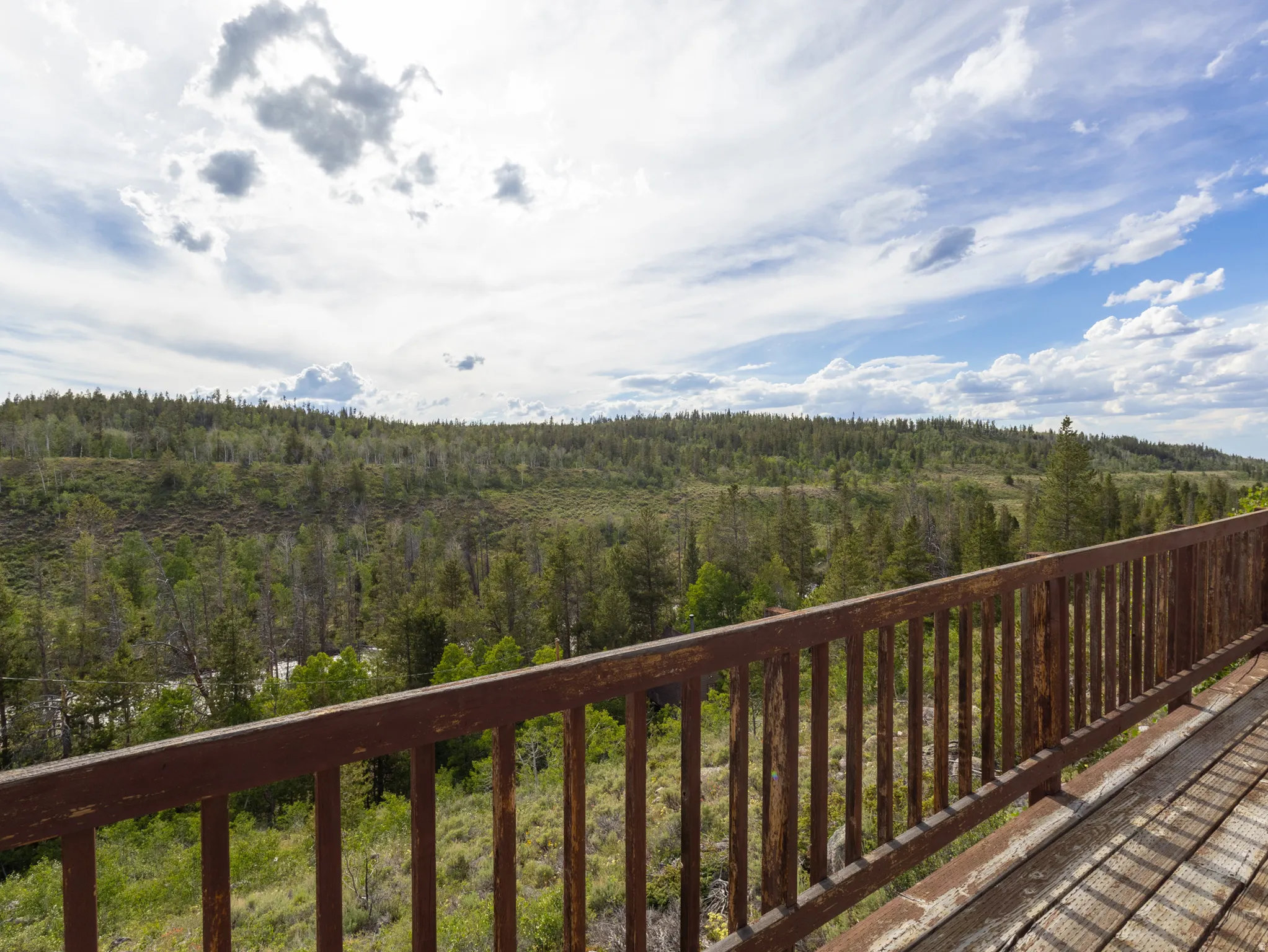 Rustic wood-finish deck with slatted railing overlooking a forested landscape