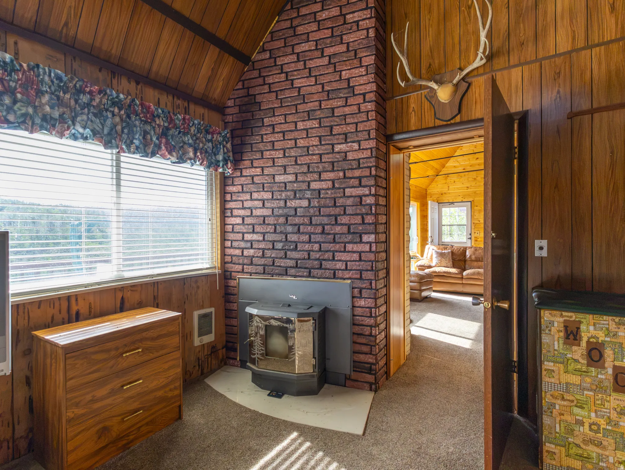 Brick fireplace with wood-burning insert, wood-paneled walls and ceiling, and carpeted flooring