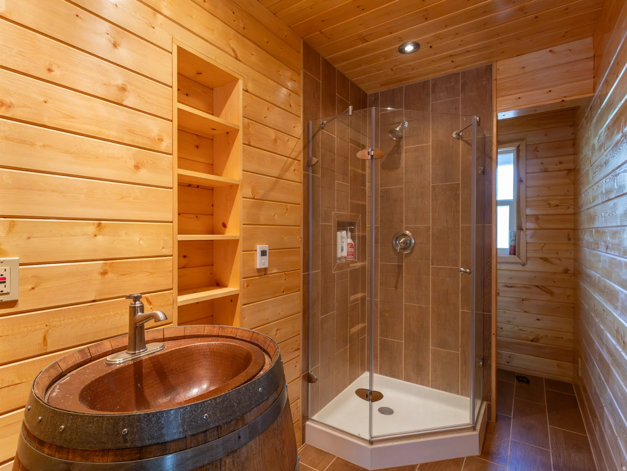 Bathroom featuring natural wood plank walls and ceiling, a barrel vanity with an oval copper sink, a glass-enclosed corner shower with tiled walls, and recessed lighting