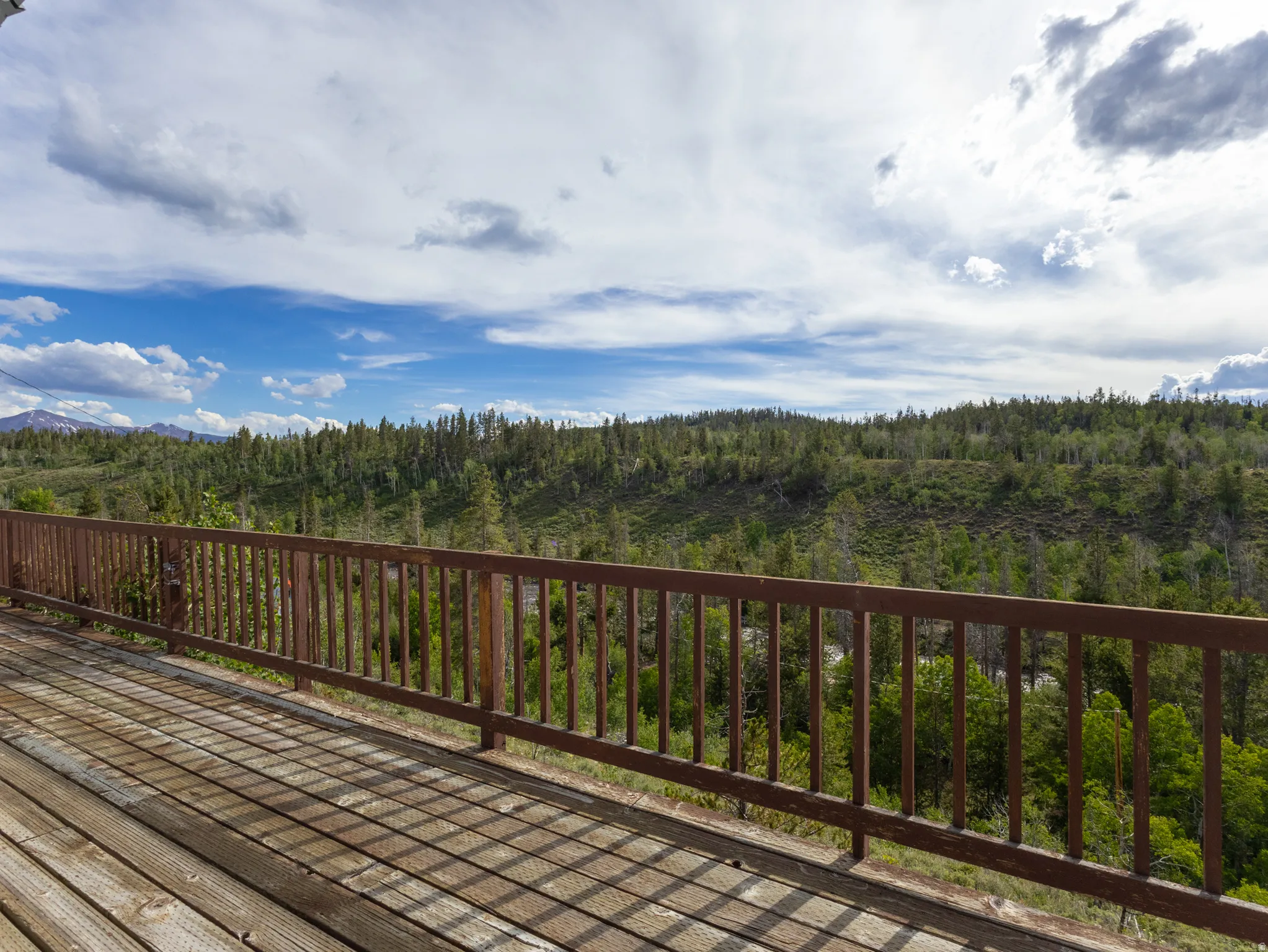 Expansive wood deck with a durable railing system, surrounded by a natural landscape of mature trees and distant mountains