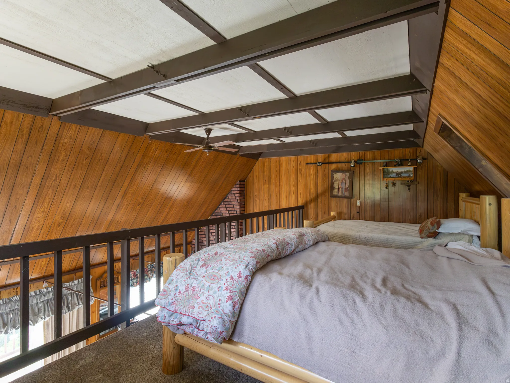 Wood-paneled loft area featuring a dark wood railing, exposed ceiling beams, a ceiling fan, and sloped wood-finish walls