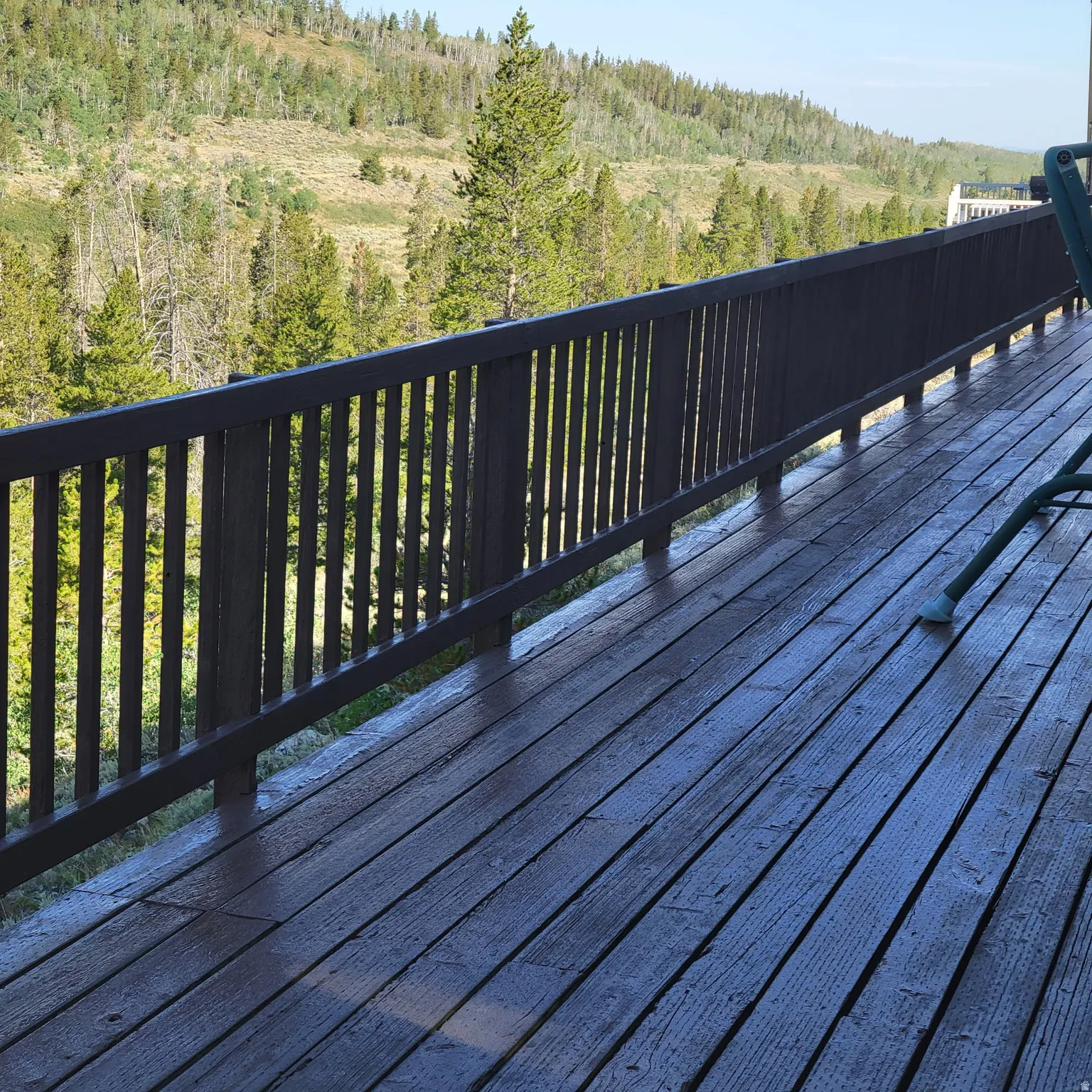 Wood-finish deck with a dark railing and expansive mountain and forest scenery