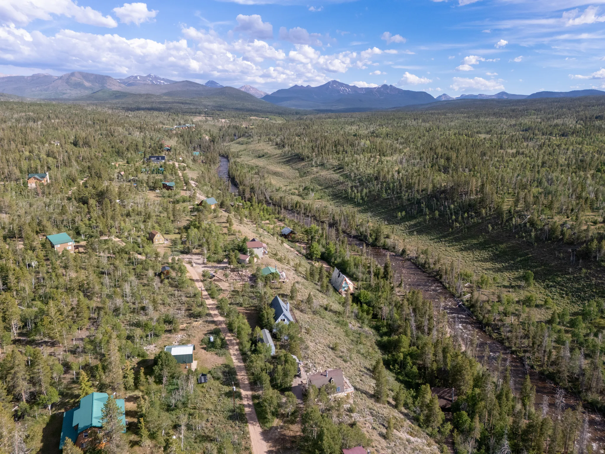 Expansive aerial landscape featuring a winding river, dense evergreen forests, scattered residential structures, and distant mountain ranges