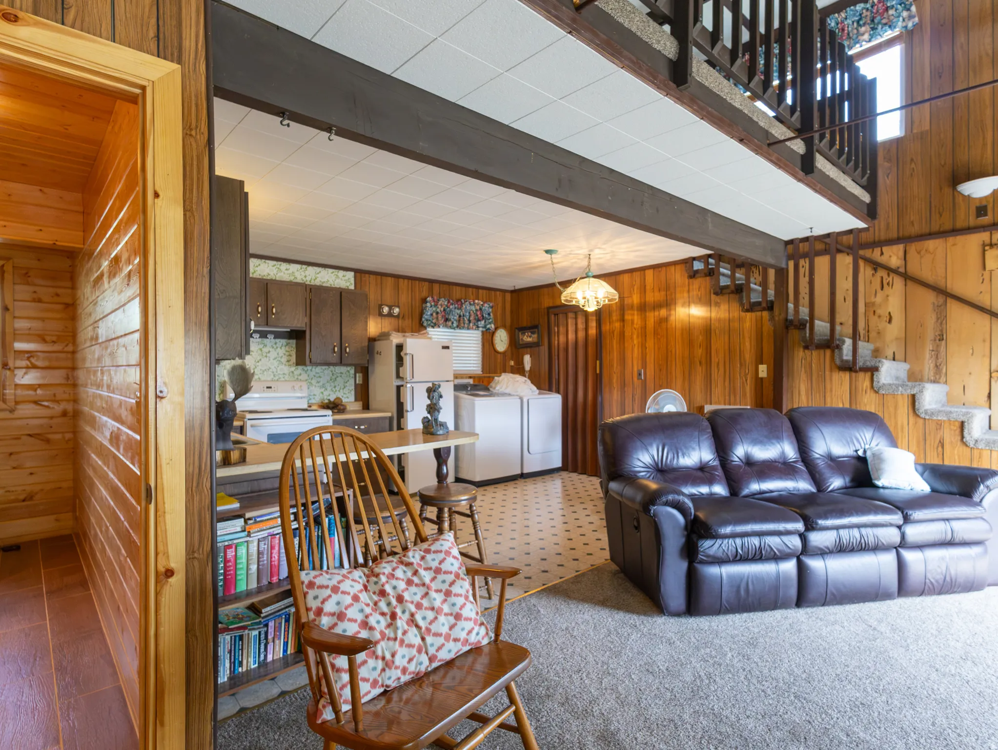 Open-concept interior featuring wood paneling, a kitchen area with dark cabinetry, and an upper-level loft with a coordinating railing