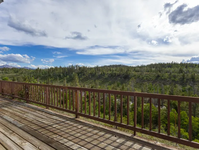 Expansive wood deck with a durable railing system, surrounded by a natural landscape of mature trees and distant mountains