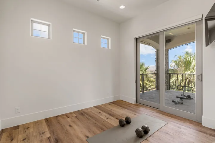 Spacious interior room featuring wood-finish flooring, high ceilings with recessed lighting, and a sliding glass door opening to a private balcony