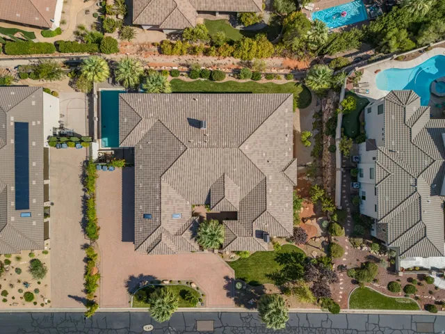 Expansive property featuring a tiled roof, a large swimming pool, mature palm trees, a brick paver driveway, and varied landscaping