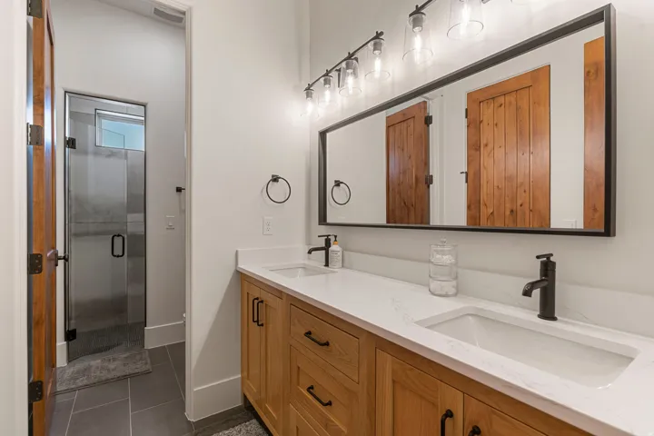 Dual vanity featuring wood-finish cabinetry, white countertops, and matte black fixtures