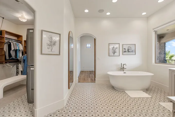 Spacious bathroom featuring patterned floor tiling, a freestanding soaking tub with a floor-mounted faucet, and a large window