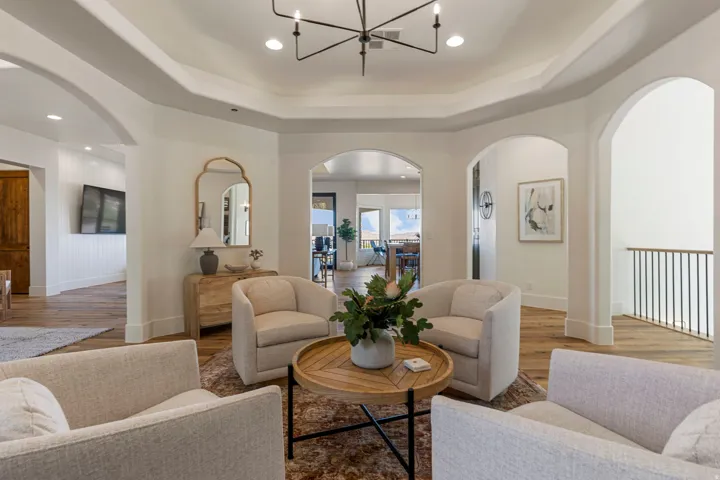 Open living area featuring wood-finish flooring, a tray ceiling with a contemporary chandelier, and multiple arched doorways