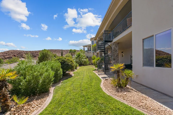Landscaped backyard featuring a winding lawn, mature desert plantings, and a spiral staircase providing access to an upper-level balcony