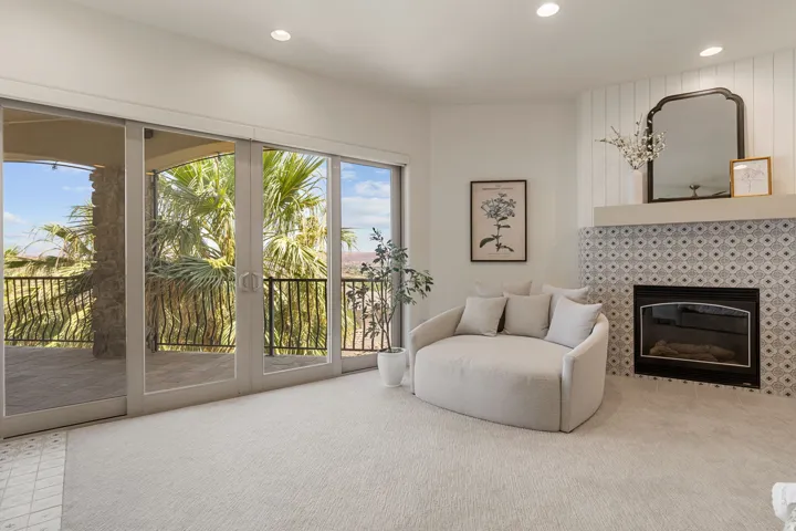 Spacious room featuring multiple sliding glass doors opening to an outdoor balcony with a wrought iron railing, a fireplace with patterned tile surround and white mantel, recessed lighting, and light-colored carpeting