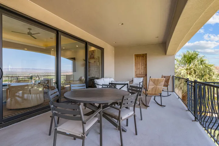 Expansive covered balcony featuring a textured concrete floor, black wrought iron railing, and a rustic wood door