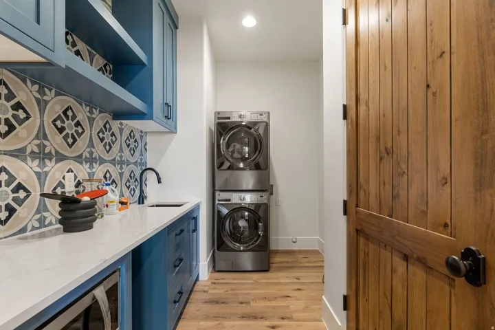 Laundry area featuring custom blue cabinetry with open shelving, a white countertop, patterned tile backsplash, and a matte black faucet