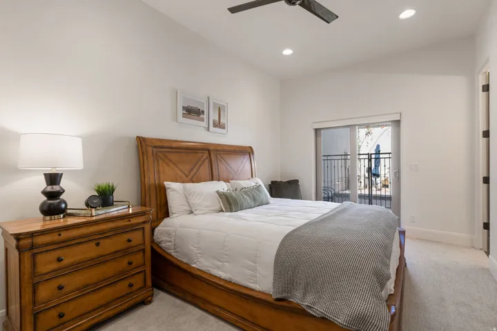 Vaulted ceiling with recessed lighting and a ceiling fan, plush carpet flooring, and a sliding glass door leading to an exterior balcony with wrought iron railing