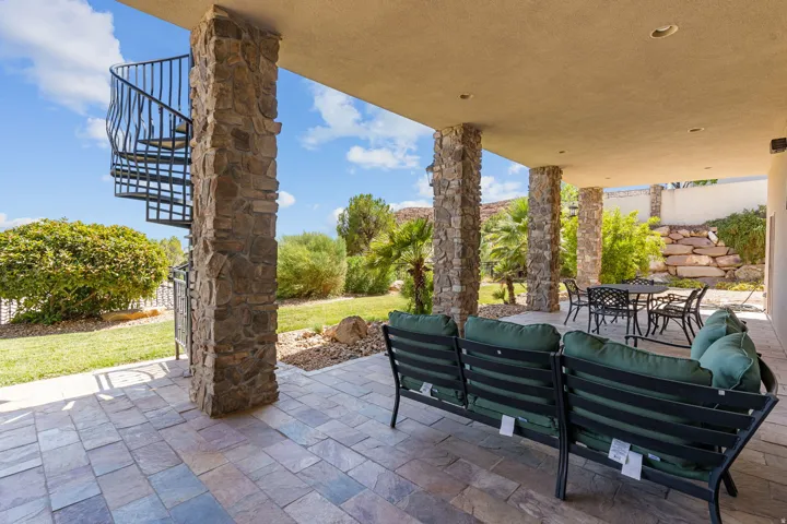 Expansive covered patio featuring stone-clad columns, a spiral staircase, and stone paver flooring