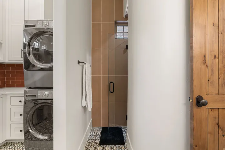 Laundry area featuring stacked stainless-steel appliances, white cabinetry, and a red subway tile backsplash