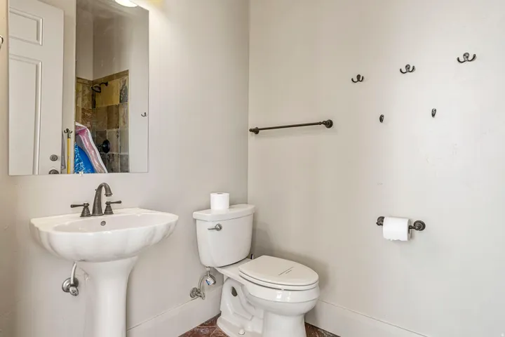 Bathroom featuring a white pedestal sink with dark bronze fixtures, a white toilet, and tile flooring