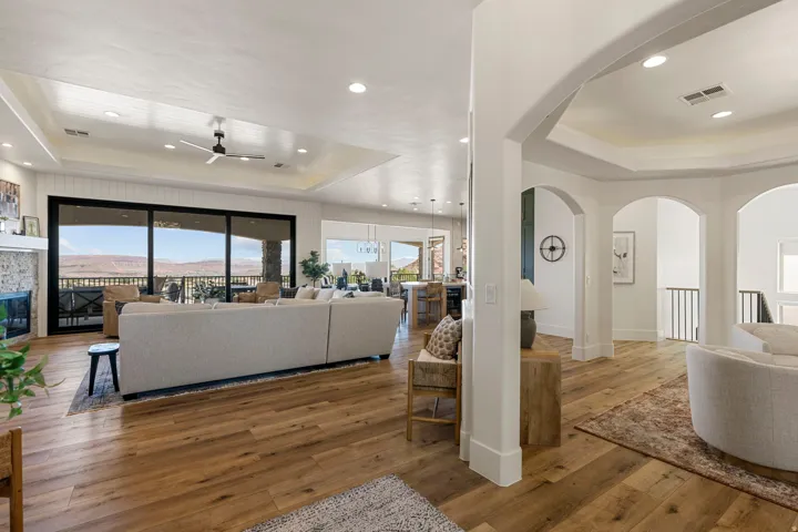 Spacious living area featuring wood-finish flooring, a stone-faced fireplace, and a tray ceiling with recessed lighting