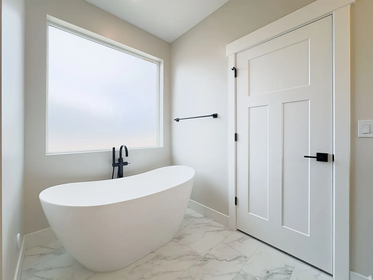 Freestanding soaking tub with matte black floor-mounted faucet, complemented by large format marble-look floor tiles