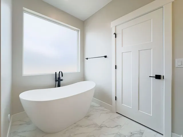 Freestanding soaking tub with matte black floor-mounted faucet, complemented by large format marble-look floor tiles
