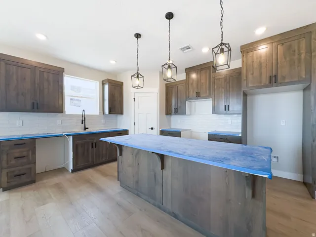 Spacious kitchen featuring wood-finish cabinetry, a large central island, subway tile backsplash, and a modern black faucet