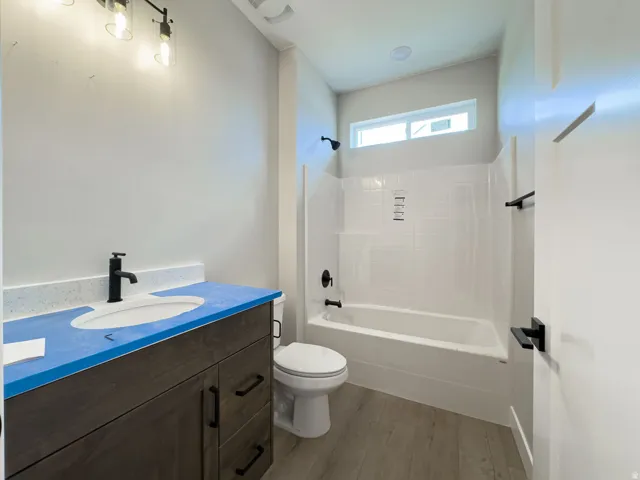 Bathroom featuring a wood-finish vanity with a built-in sink, matte black fixtures, a white tile-surround bathtub, and wood-finish flooring