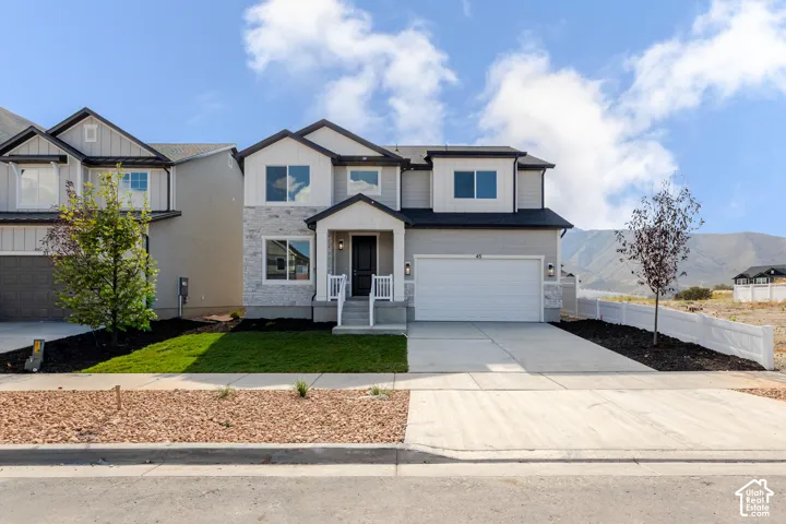 Two-story exterior featuring a stone veneer facade, horizontal siding, attached two-car garage, covered entryway, and mountain backdrop