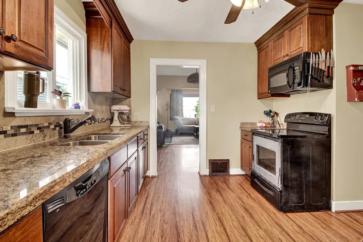 Kitchen featuring wood-finish flooring, granite-style countertops, wood cabinetry, stainless steel double basin sink, and a multi-tone tile backsplash