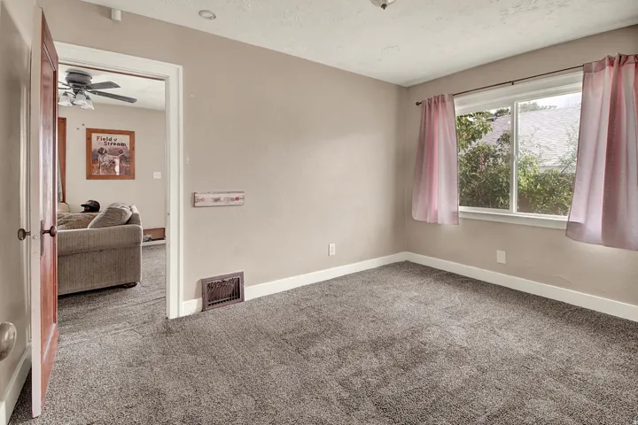 Carpeted room featuring a double-hung window, light beige wall paint, white baseboards, and a wooden interior door