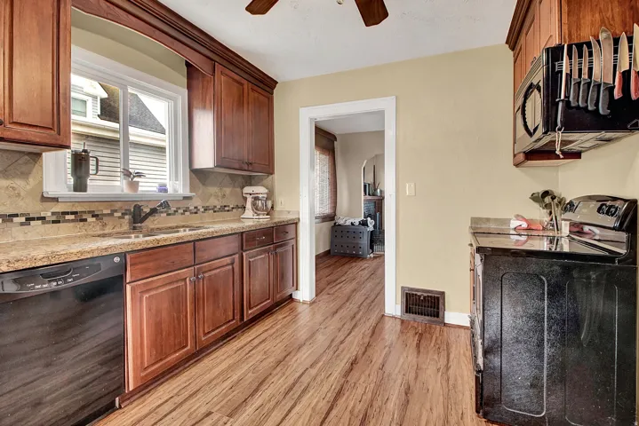 Kitchen featuring wood-finish flooring, wood cabinetry with crown molding, light-toned countertops, and a mosaic tile backsplash