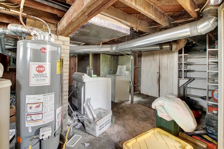 Basement utility area featuring a hot water heater, exposed wood joists, brick detailing, and permanent shelving