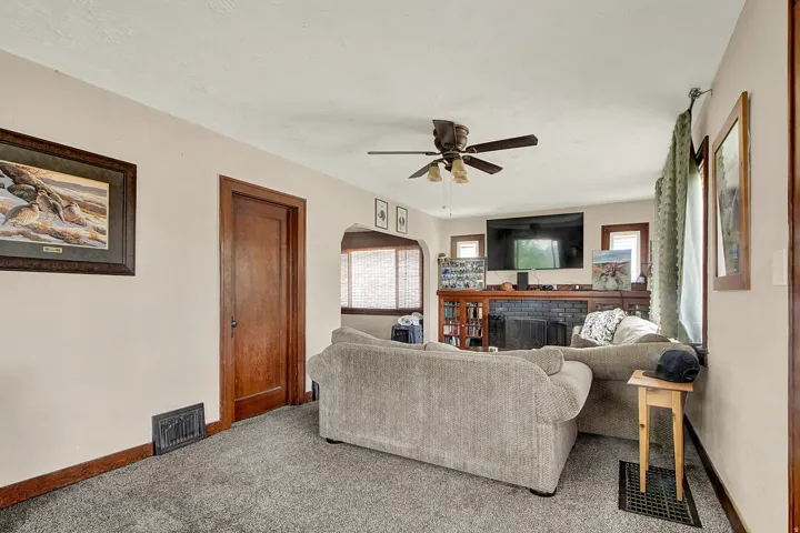 Living area featuring a textured gray carpet, light neutral walls, and a fireplace with a dark brick surround and wood mantle