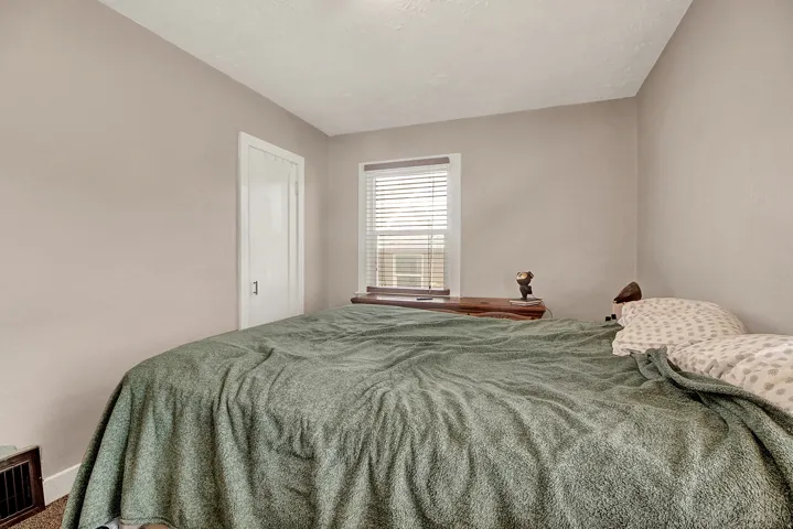 Bedroom featuring light neutral wall paint, white trim, a single window with blinds, and white interior door with dark hardware