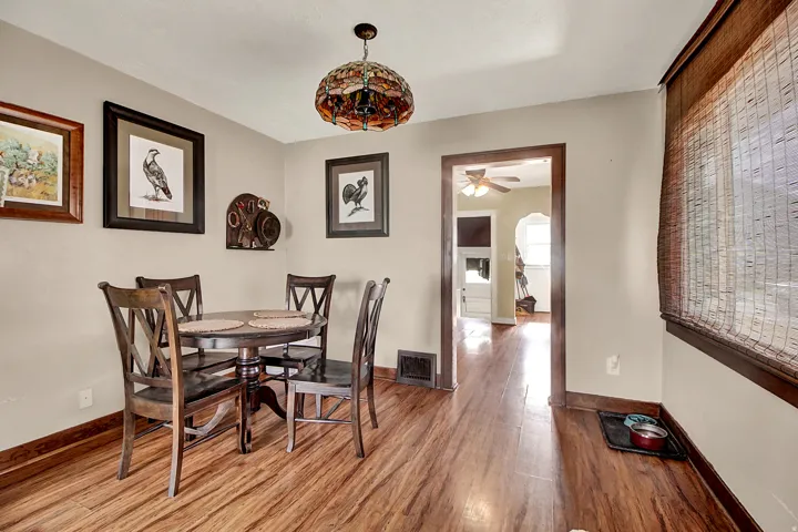 Dining area featuring wood-finish flooring, a decorative stained-glass pendant light fixture, and a window with a woven shade
