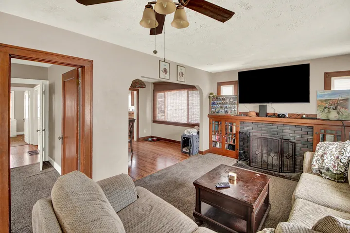 Living area featuring a tiled fireplace with an ornate screen, built-in shelving, wood-trim windows, and an arched doorway