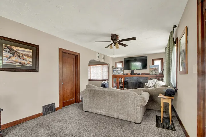 Living area featuring carpet flooring, a wood-finish door, and a ceiling fan
