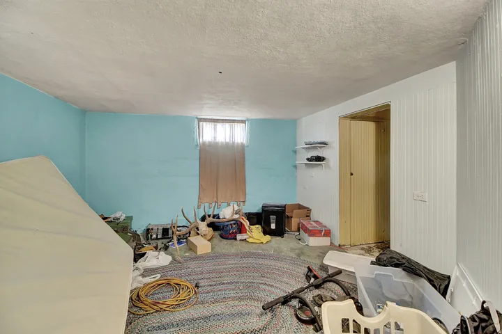 Finished lower level space featuring a window, light blue painted walls, a textured ceiling, built-in shelving, and a doorway