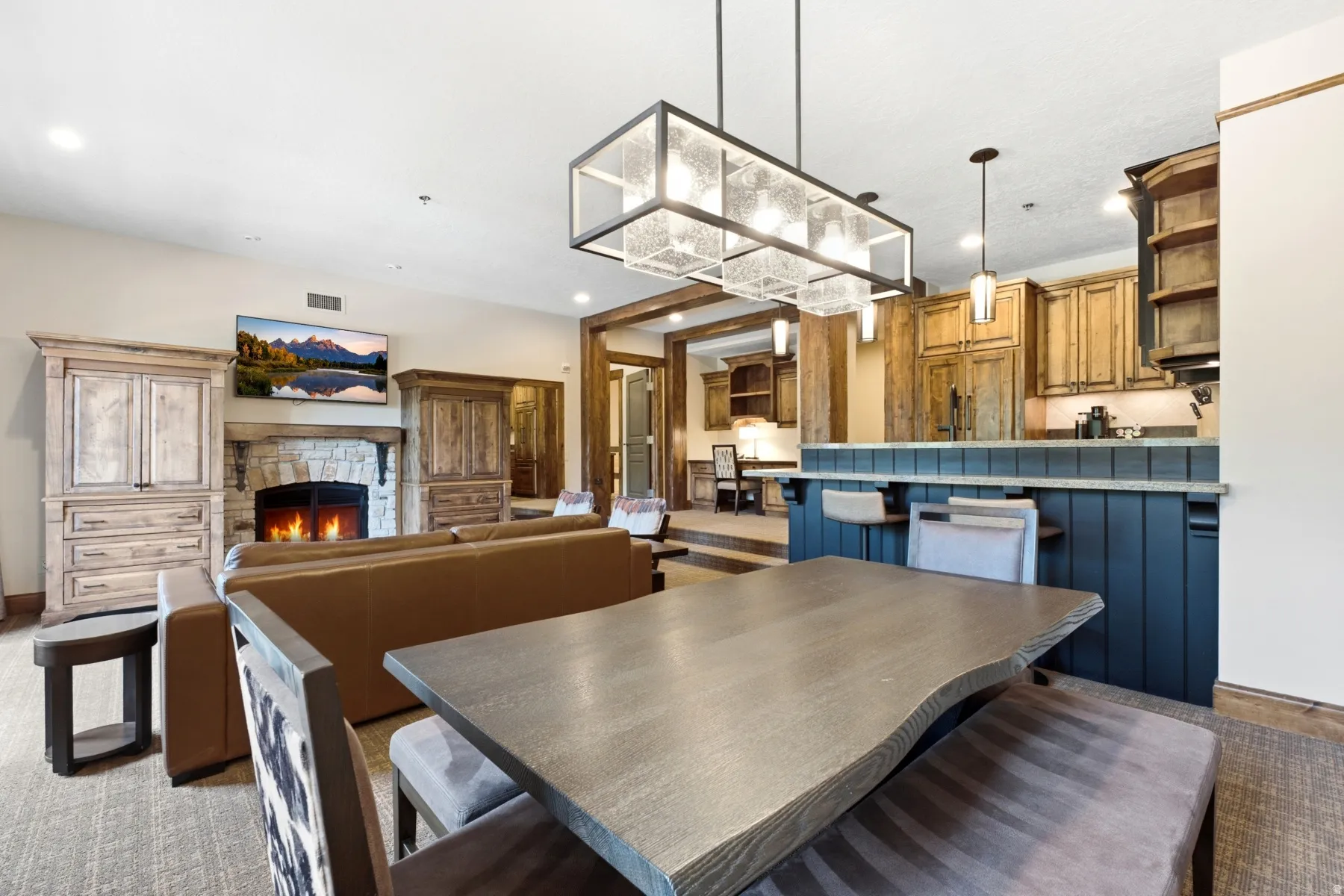 Open-concept living space featuring a stone-surround fireplace, built-in wooden cabinetry, recessed lighting, and a prominent kitchen island with seating