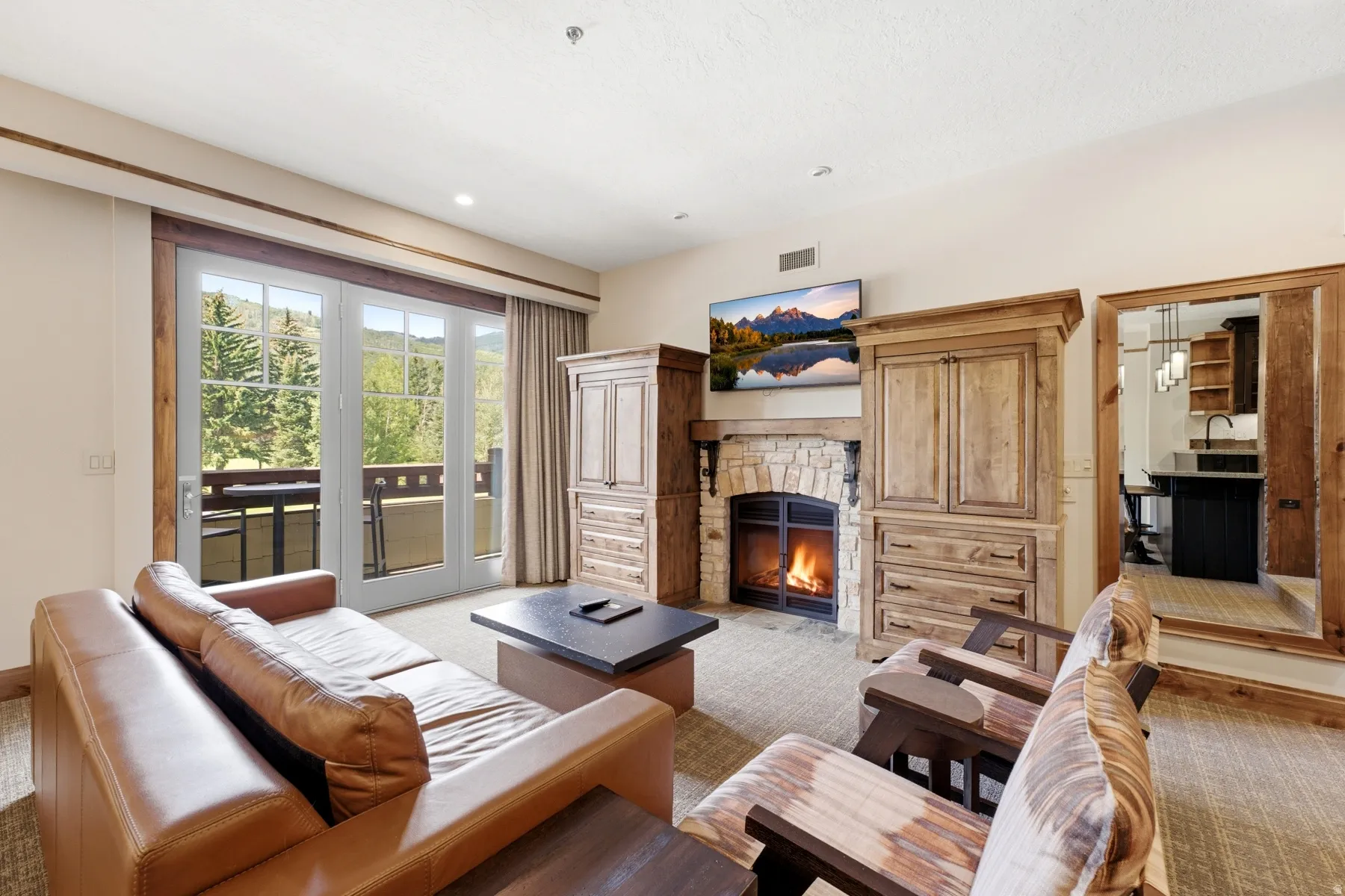 Living area featuring a stone-surround fireplace, custom wood cabinetry, and a large glass-paned door opening to an outdoor balcony