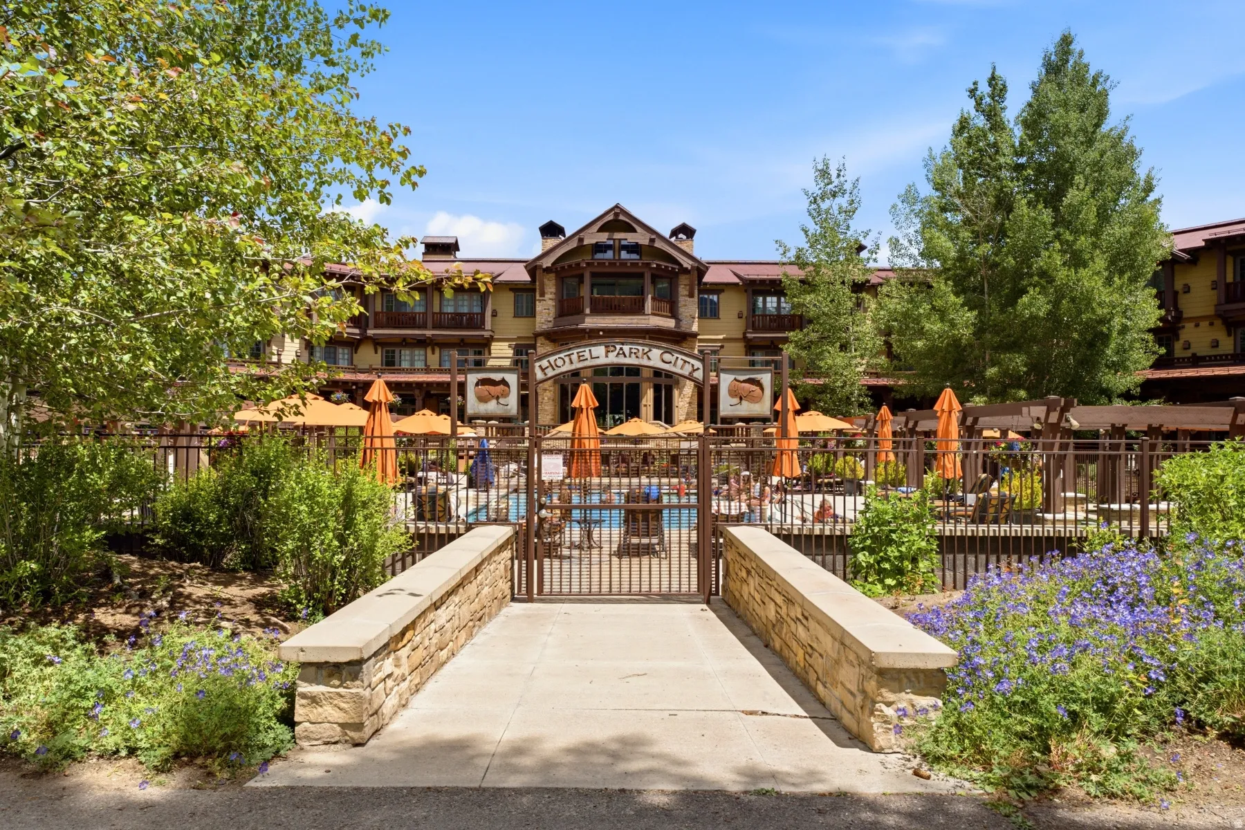Stone-clad architectural exterior featuring a swimming pool area with numerous orange umbrellas and a surrounding privacy fence