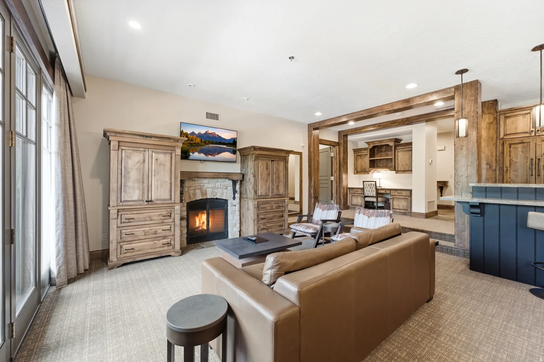 Living area featuring a stone-surround fireplace, wood-finish built-in cabinetry, exposed wood-finish beams, and a built-in wet bar with a stone countertop